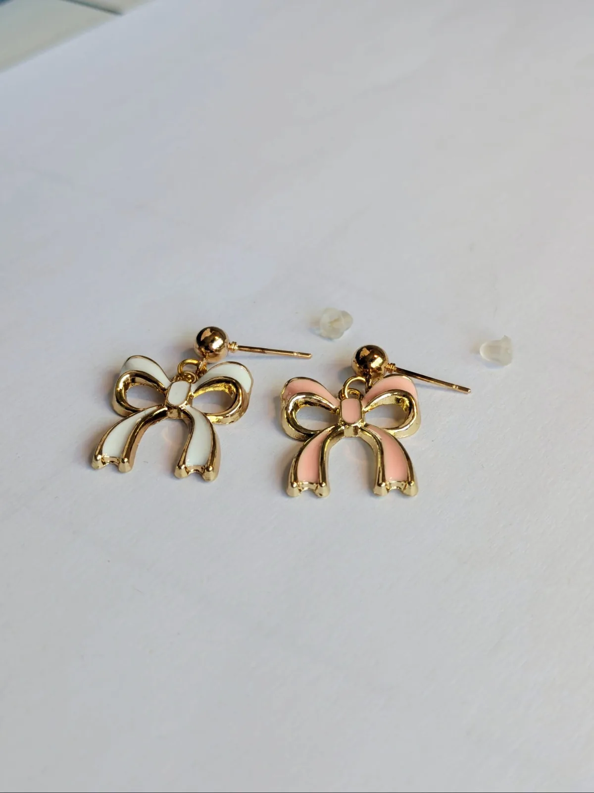Boucles d'oreilles puces nœud doré dépareillées, une en émail blanc et une en émail rose