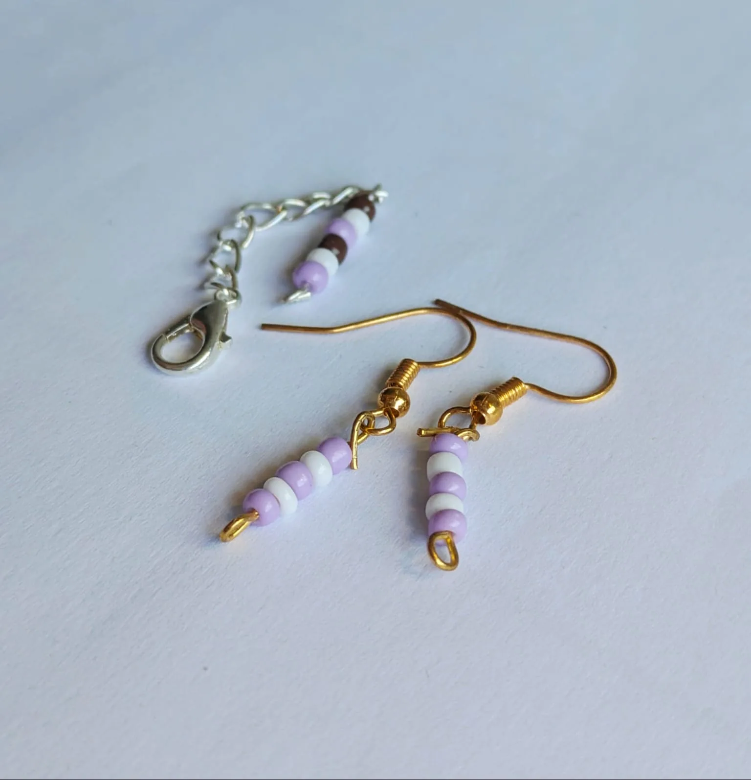 Boucles d'oreilles barrette en perles lilas et blanches présentées avec une chaîne d'extension assortie en perles marron, blanches et lilas