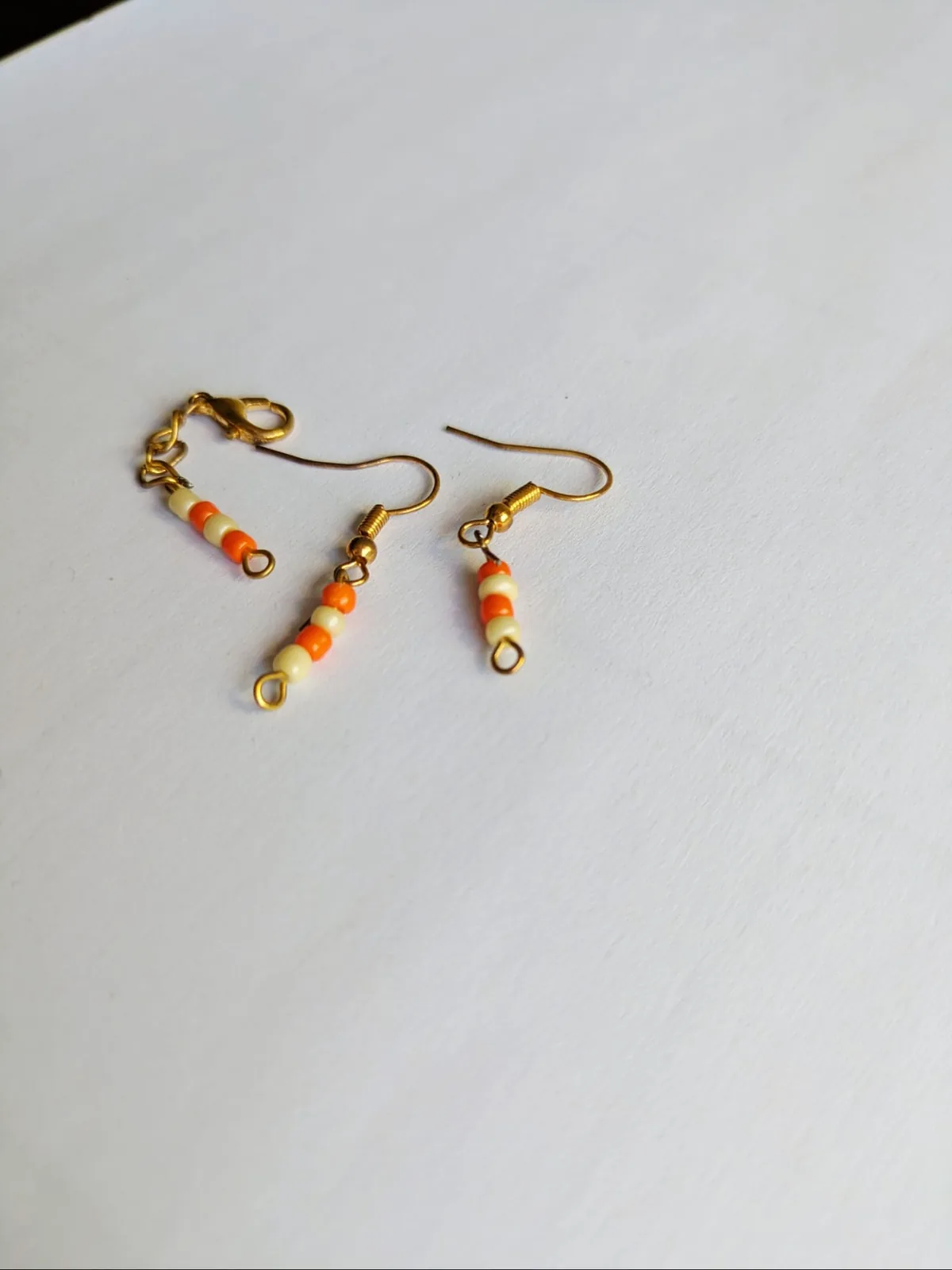 Boucles d'oreilles barrette en perles orange et crème présentées avec une chaîne d'extension assortie